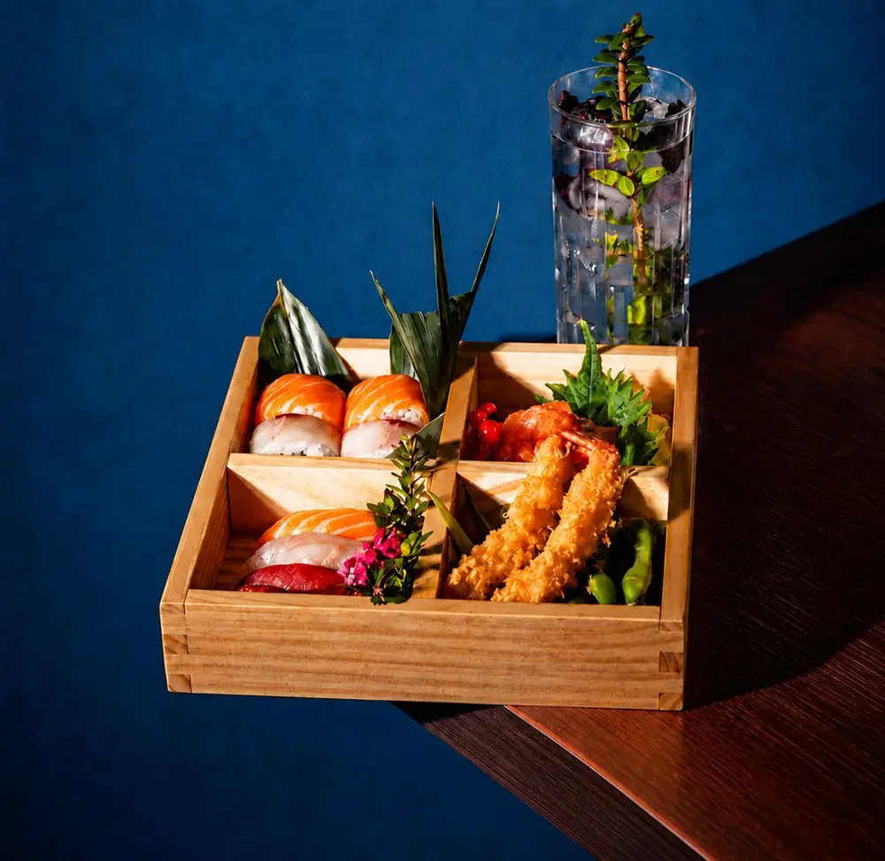 Bento dell'aperitivo Ukiyo con nigiri misti, tempura di gamberi ed edamame, accanto a un cocktail