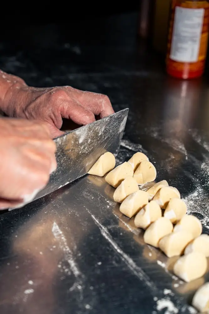 Il cuoco taglia l'impasto dei ravioli con la mannaia
