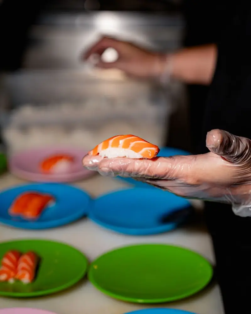 Nigiri al salmone preparato al banco, con i piattini colorati del kaiten