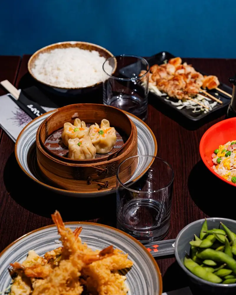 Tavola apparecchiata con shumai al vapore, riso, spiedini, tempura ed edamame